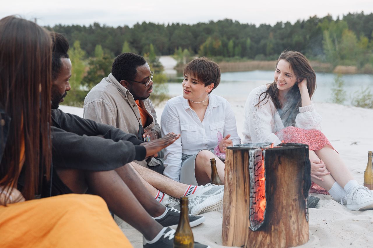 A group of friends relaxes around a bonfire on a sandy beach, enjoying a summer day.